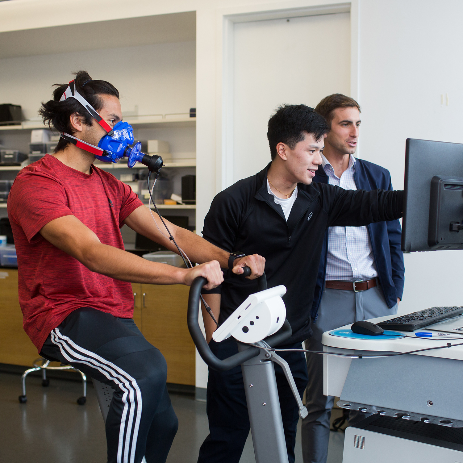 research being conducted on one person hooked up to a bike machine with two people looking at data behind a computer screen